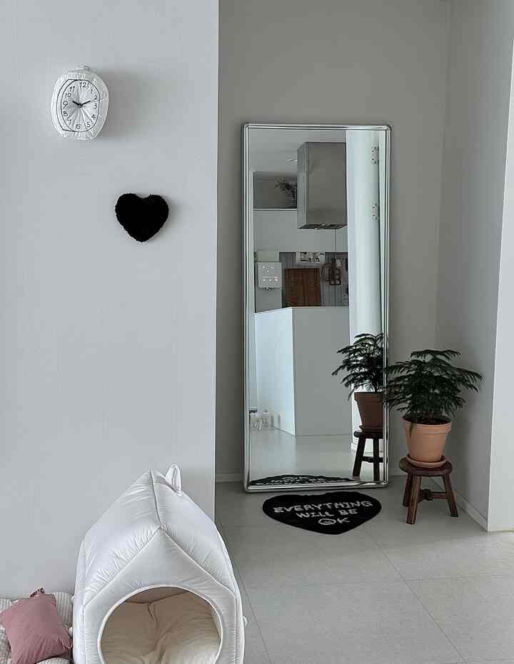Natural living room with white walls and floors, accented by a full-length mirror and a pet house