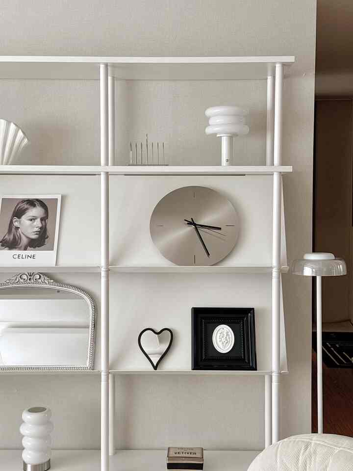 白とモダンな色調のリビングの棚、中央に金属製の時計と黒い額縁が配置された印象的なインテリア空間