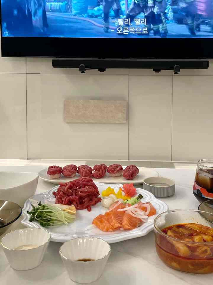 白を基調としたリビング、壁に取り付けられたテレビとサウンドバー、テーブルには盛り付けられた料理が並ぶ夜のムードのある空間