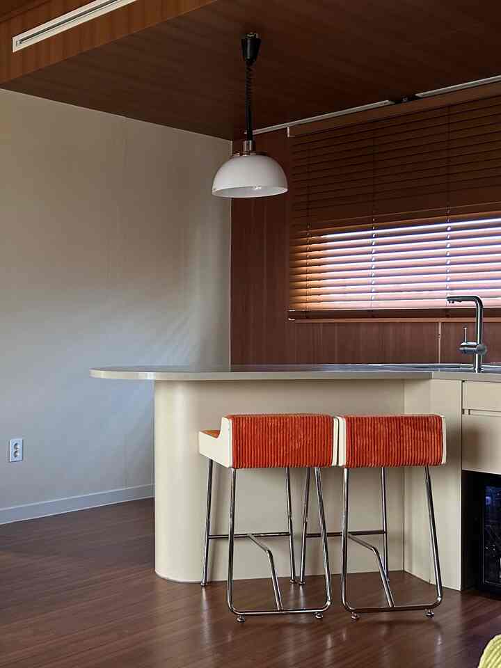 Beige kitchen featuring wood blinds and orange bar stools in a natural modern kitchen space