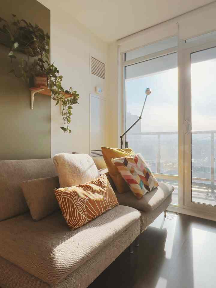 A natural-toned living room with white and beige hues, featuring a large window and sofa illuminated by warm sunlight