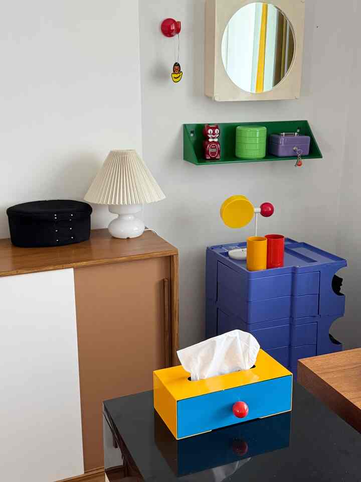 白い壁と木目調のキャビネット、青いモジュラー収納ユニット、多彩な小物が配置されたモダンでミニマルなインテリア空間