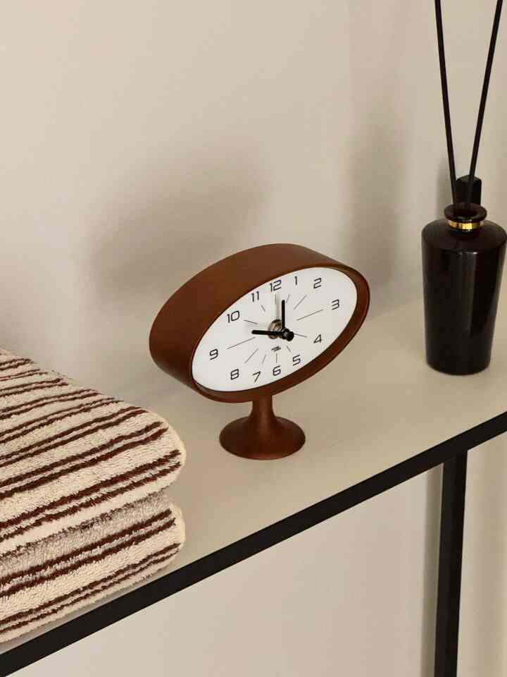 A modern side table featuring a brown simple table clock, striped towels, and a diffuser