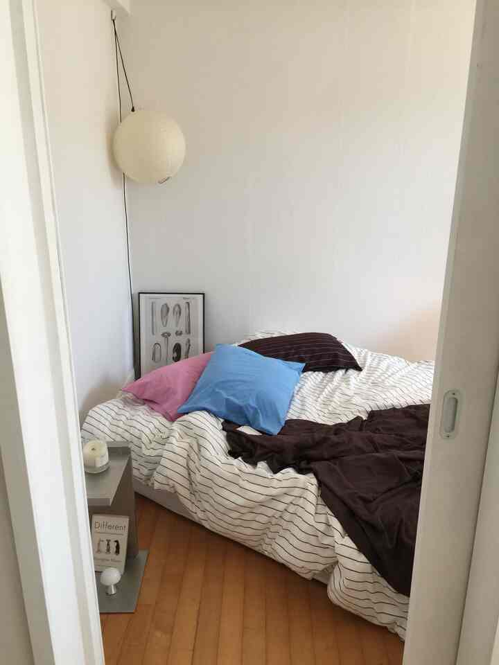 白と木目調の小さな寝室、ベッドとサイドテーブルが配置された落ち着いた空間