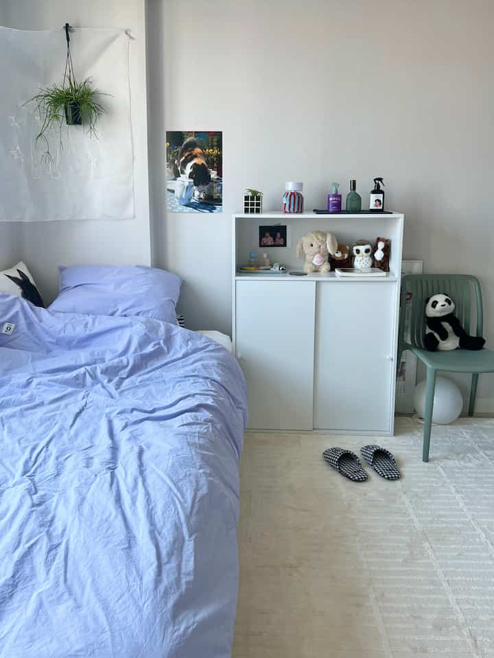 ラベンダー色調の寝室、白い本棚と自然な植物の装飾がある落ち着いた空間