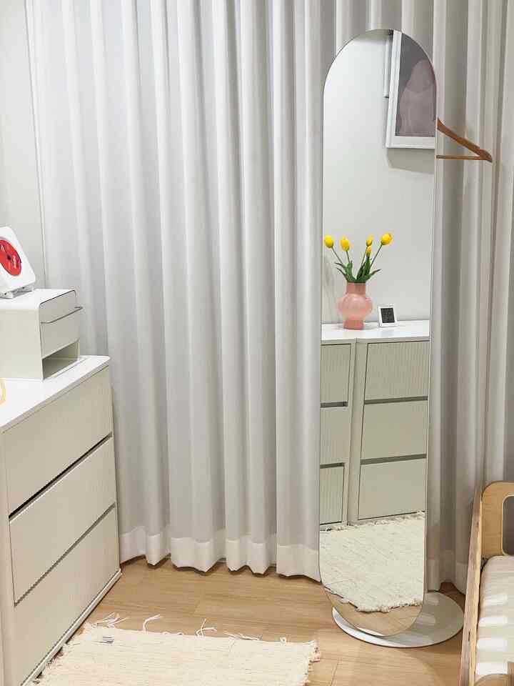 明るいホワイトと木目調のウォークインクローゼット、全身鏡と白いチェスト、ハンガーが配置されたシンプルでミニマルなインテリア