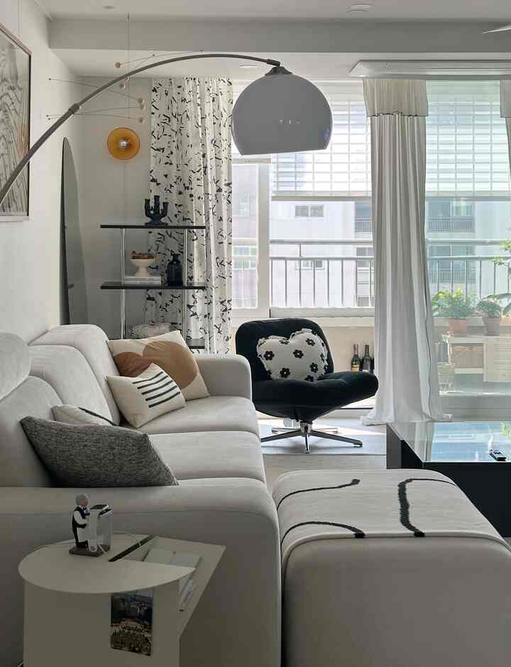 A white and black toned living room featuring a cream modular sofa, black armchair, side table, and curtains for a cozy atmosphere