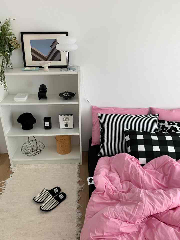 Simple single household bedroom with pink bedding and white walls and shelving