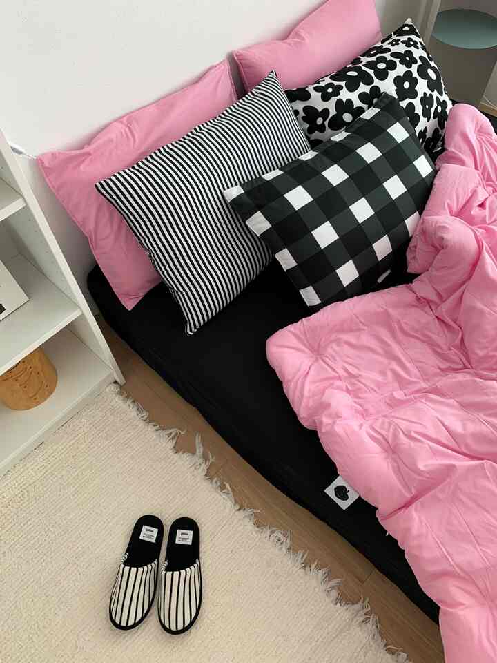Pink-toned bedroom featuring a cozy bed with black and white patterned pillows and a textured rug