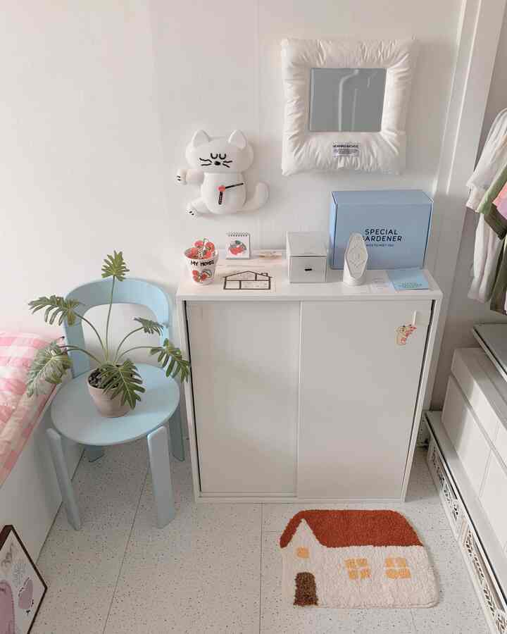 白と淡い青の色調の子供部屋、収納キャビネットとパステルブルーの椅子、家の形のラグが配置された、落ち着いたシンプルな印象的な空間