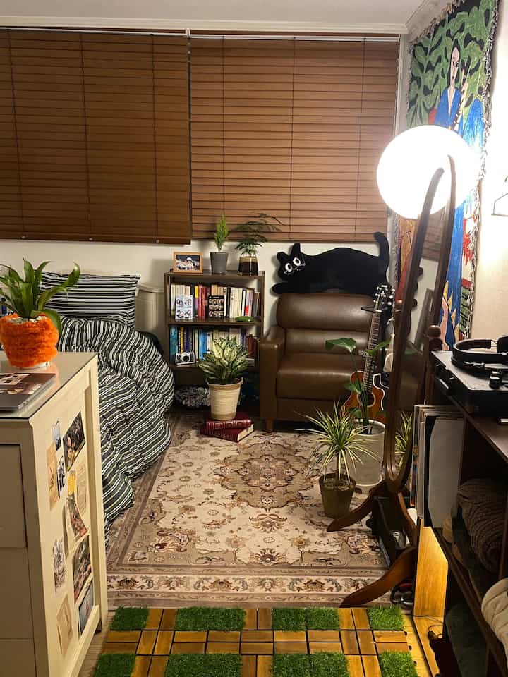 ブラウンのウッドブラインドと大きなラグがある、猫のぬいぐるみとレザーのリクライナーを備えた居心地の良い一人暮らしの寝室