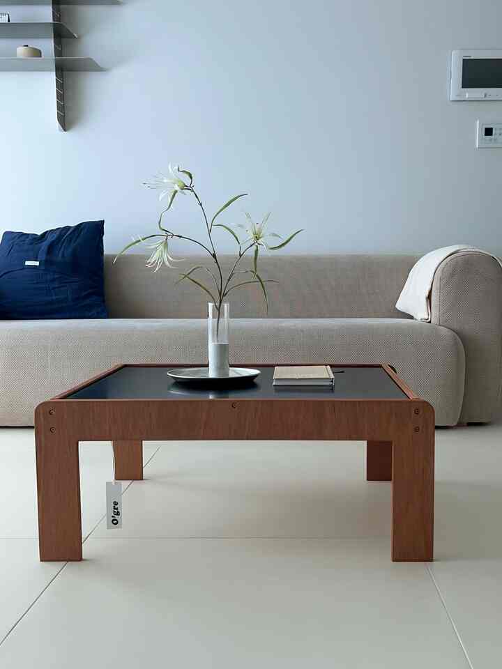 ベージュのソファと木製のコーヒーテーブルが配置されたシンプルでナチュラルなリビング、透明な花瓶で飾られている