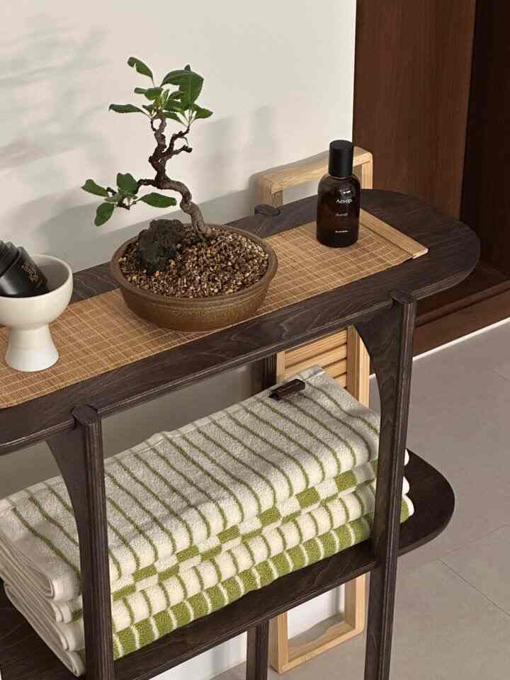 ナチュラルカラーの棚にタオルと小さな植物が置かれた清潔感のあるバスルームアクセサリーの空間