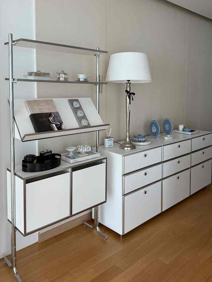 ホワイトとウッドトーンの縦長のキッチンスペース、収納キャビネットとフロアランプが配置された印象的なインテリア