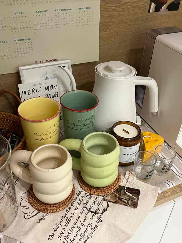 ナチュラルな木目調の背景に白い電気ケトルとカラフルなマグカップが置かれた雰囲気のあるおうちカフェ