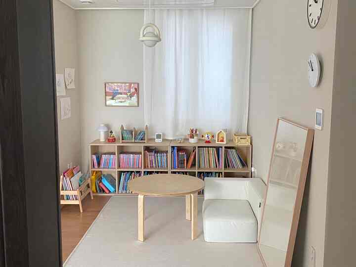 ナチュラルカラーの子供部屋、木製の丸テーブルとホワイトのコーナーソファ、絵本が並ぶ本棚が配置された暖かみのある空間