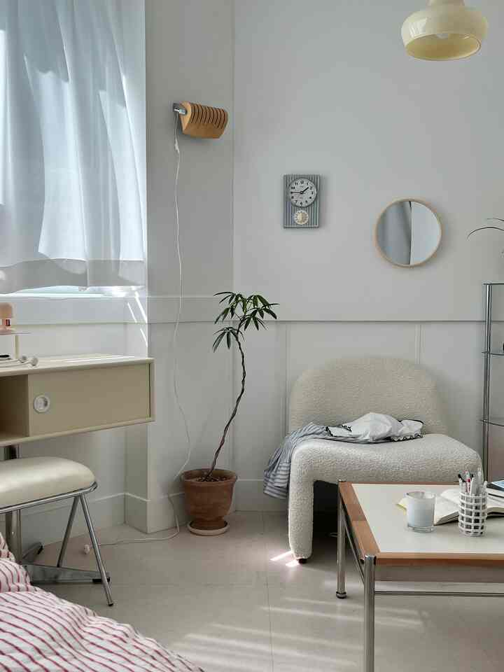 Natural white-toned living room featuring an armchair, round mirror, wall clock, and potted plant in a minimalist setting