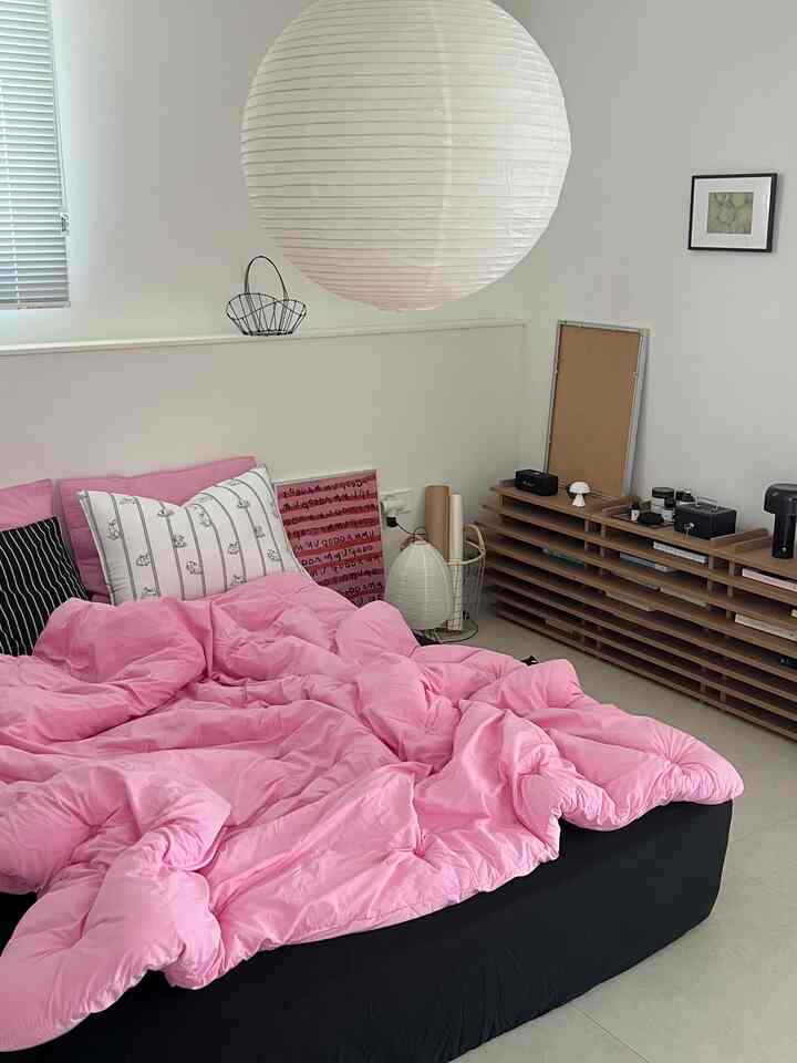 White-toned bedroom with prominent pink bedding, featuring modern furniture and pendant lighting creating a cozy atmosphere