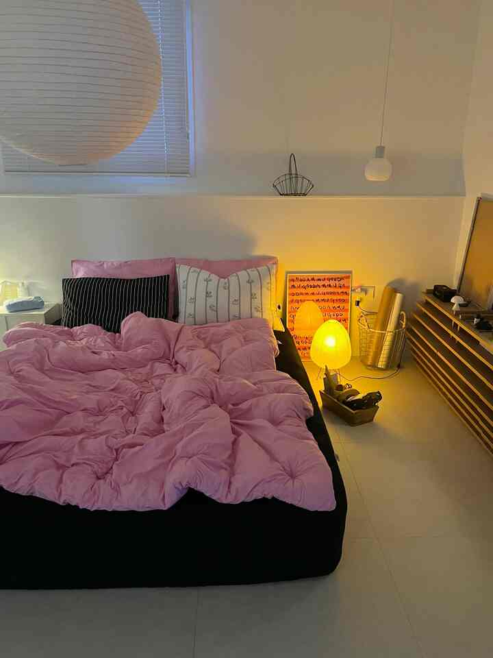 Modern bedroom featuring a black bed frame with pink bedding, warm ambient lighting, and a poster near the floor creating a cozy atmosphere