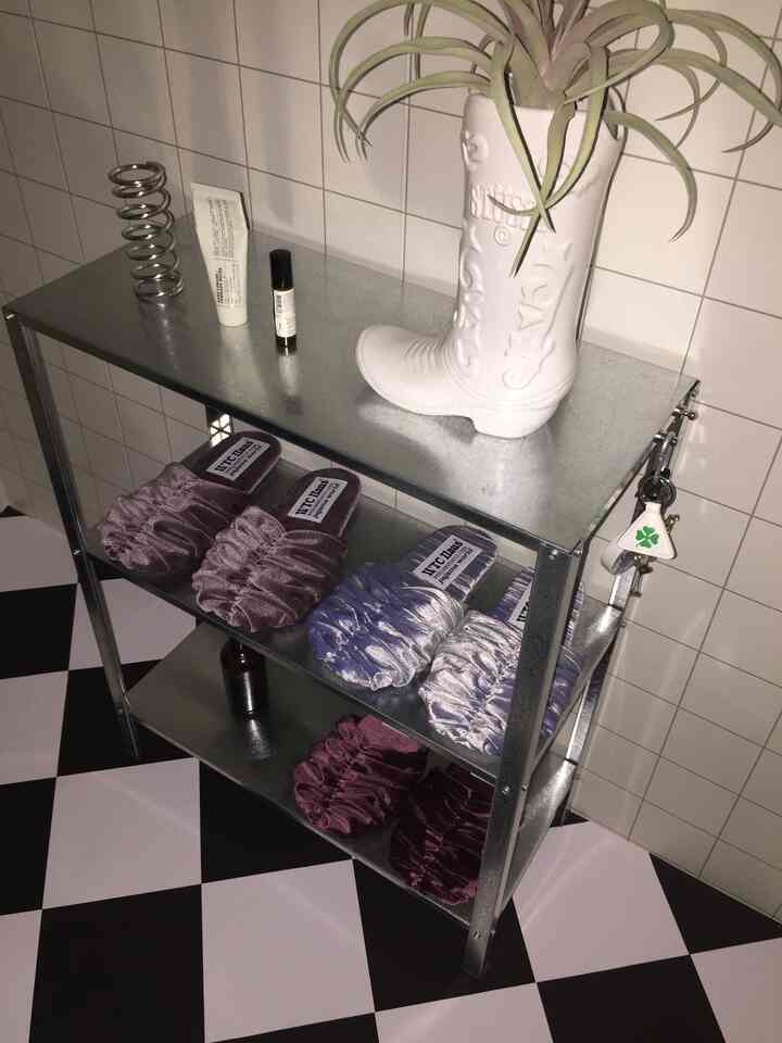 白いタイルの壁と白黒チェッカーフロアのモダンな空間、メタル製の収納棚に色とりどりのスリッパが並ぶ