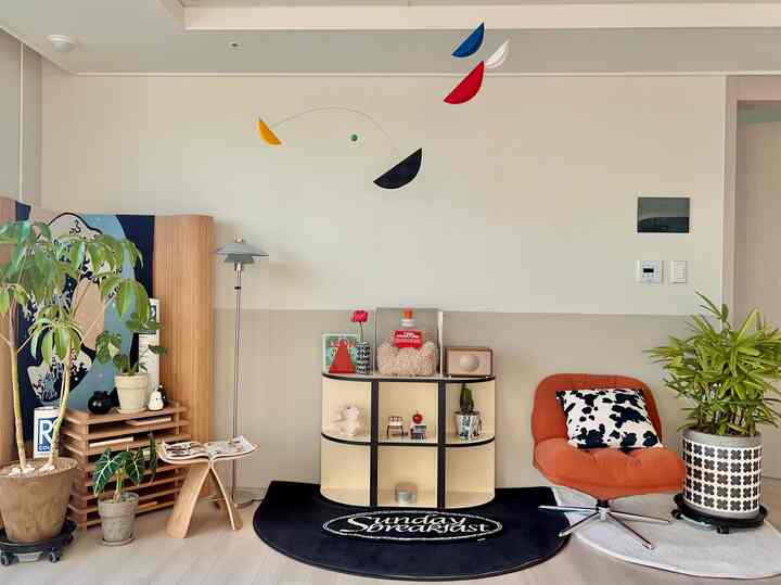 アイボリーと明るいグレーの色調のリビング、オレンジ色のラウンジチェアと植物が配置されたモダンなインテリア