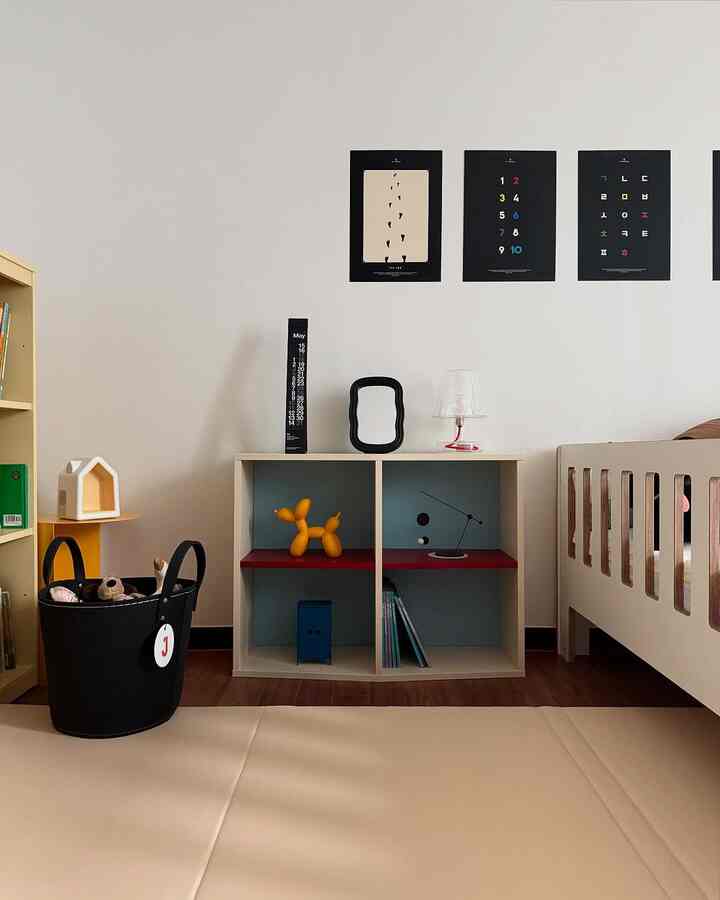 ベージュ色調の子供部屋、中央にスカイブルーとバーガンディの斜め棚とベビーベッドが配置されたシンプルでナチュラルな雰囲気のインテリア