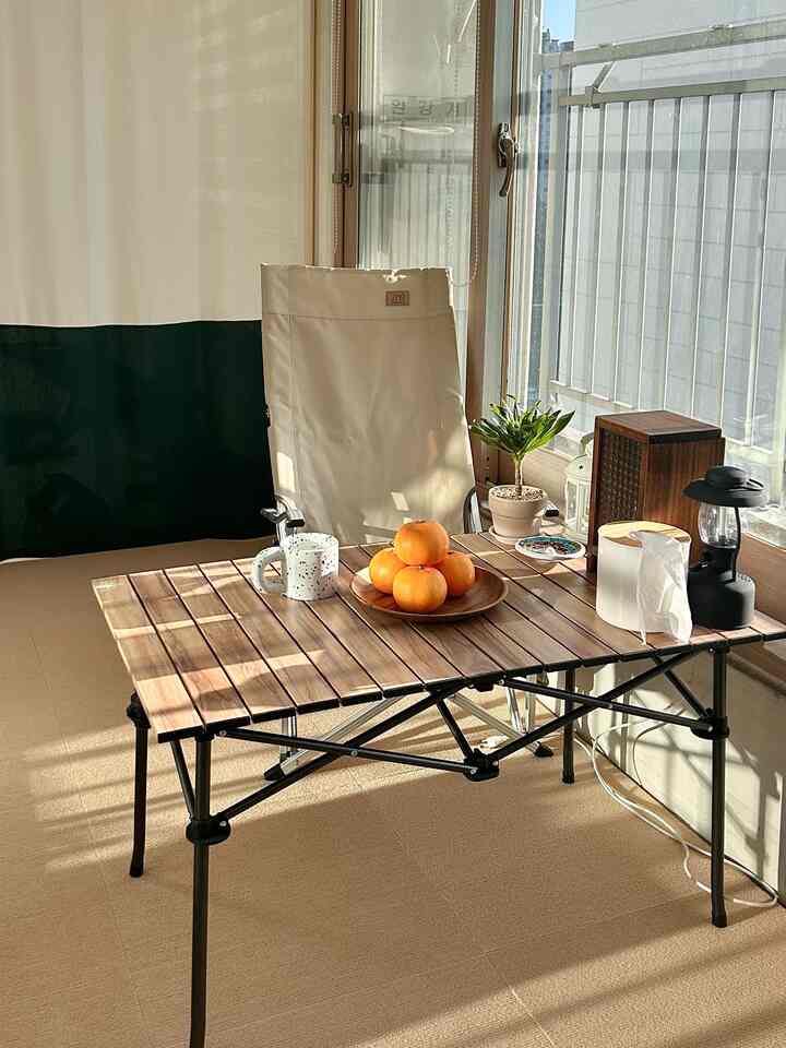 温かみのあるウッドトーンとベージュのベランダ、折りたたみアームチェアと木製テーブル、植木鉢やコーヒーマグが配置された雰囲気のあるインテリア