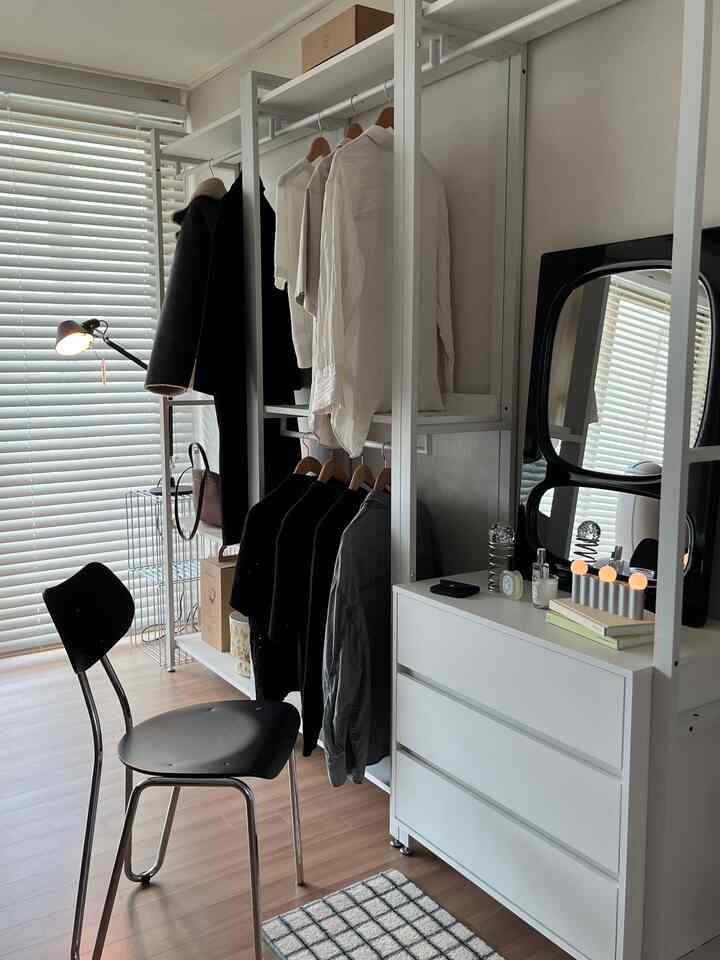 白と黒のトーンのウォークインクローゼット、衣類ラックと鏡、ドレッサー、スツールが配置されたすっきりとしたモダンな空間