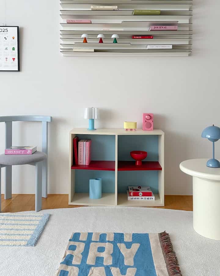 スカイブルーとバーガンディがアクセントのリビング、シンプルでモダンな棚と小物が配置された温かみのある空間