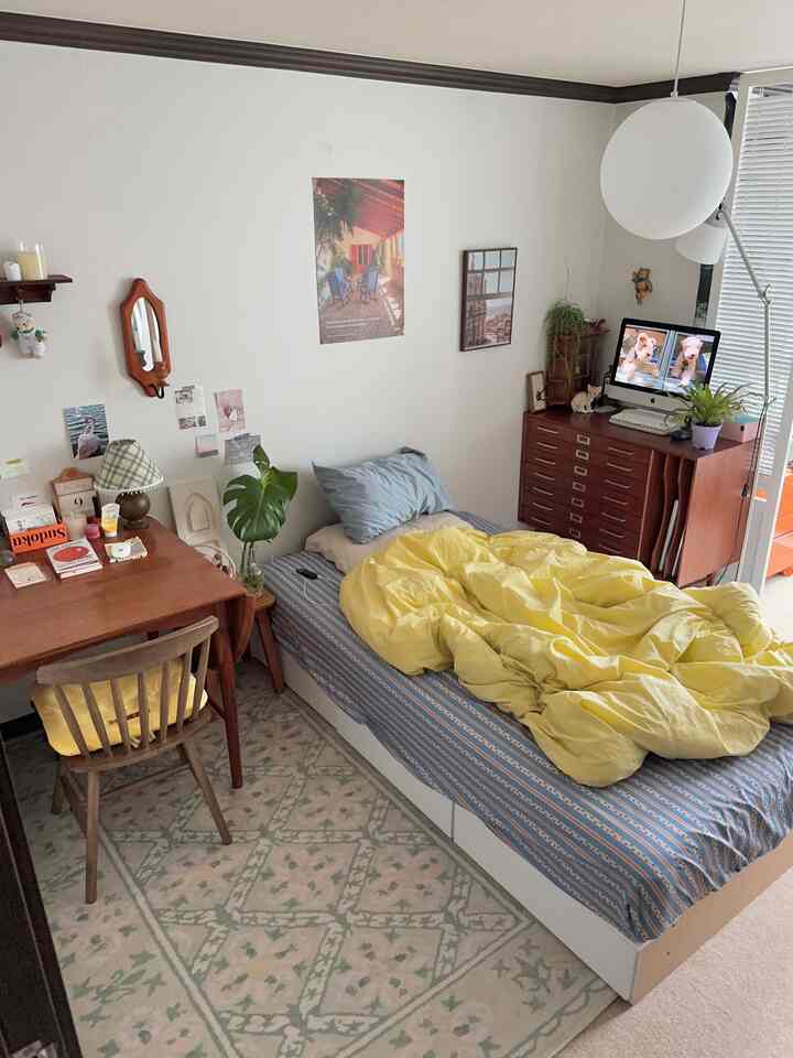 アイボリーの壁と木目調家具、黄色い寝具が配置された一人暮らし用のコンパクトな寝室スタジオ、温かみのあるヴィンテージな雰囲気のインテリア