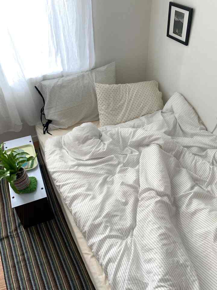 ナチュラルな色調の寝室、ストライプ柄の寝具と枕が配置された落ち着いた空間