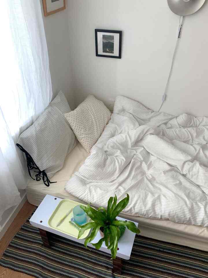 白とナチュラルカラーの寝室、ミニマルなストライプ柄の寝具と小さな額縁が配置された落ち着いた雰囲気のインテリア