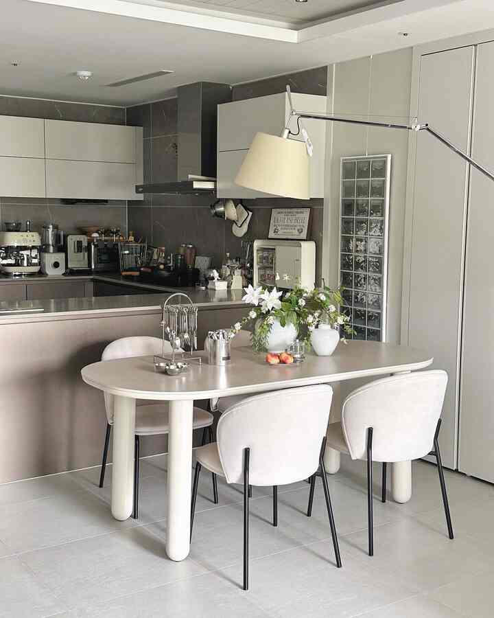 柔らかなベージュ調のキッチン、エレガントなポーセリンセラミックのダイニングテーブルとクリームベージュの椅子が配置されたモダンなフレンチスタイルのインテリア