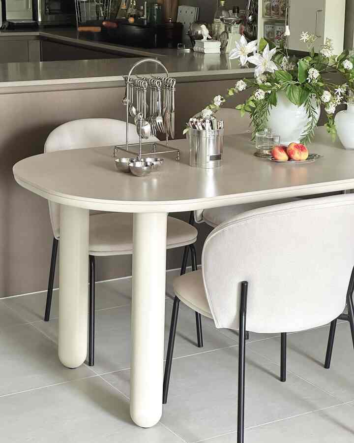 明るい白と茶色の色調のキッチンとダイニングスペース、中央のダイニングテーブルにカトラリー掛けと花瓶が配置された雰囲気のあるインテリア