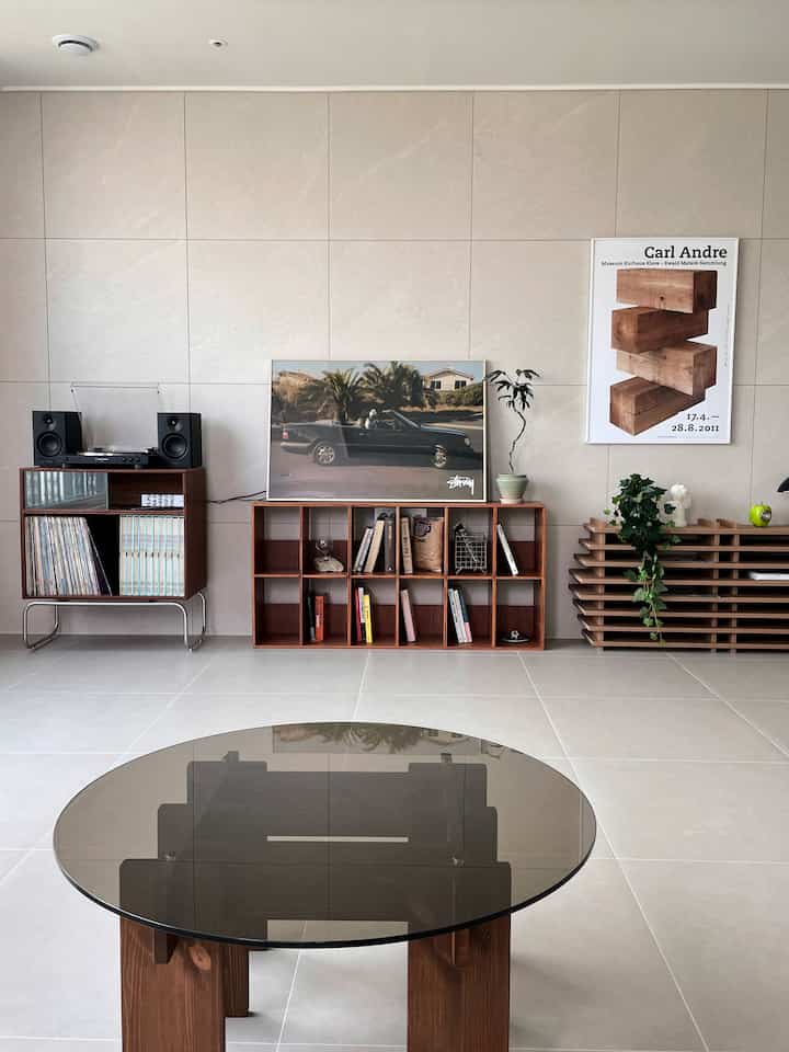 A simple living room featuring a natural wood tone round glass coffee table and wooden bookshelves