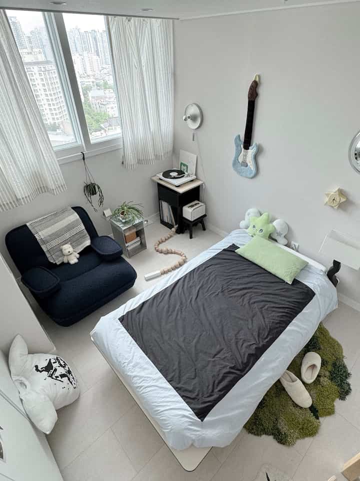 ホワイトとグレーのトーンのワンルーム寝室、ソファとベッド、ターンテーブルが調和したコンパクトな空間