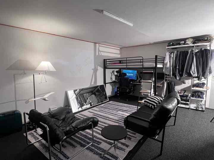 ブラック、ホワイト、シルバーのトーンのワンルーム、ロフトベッドとデスク、レザーのアームチェア、大きな横置きミラーが配置されたミッドセンチュリーモダンなインテリア