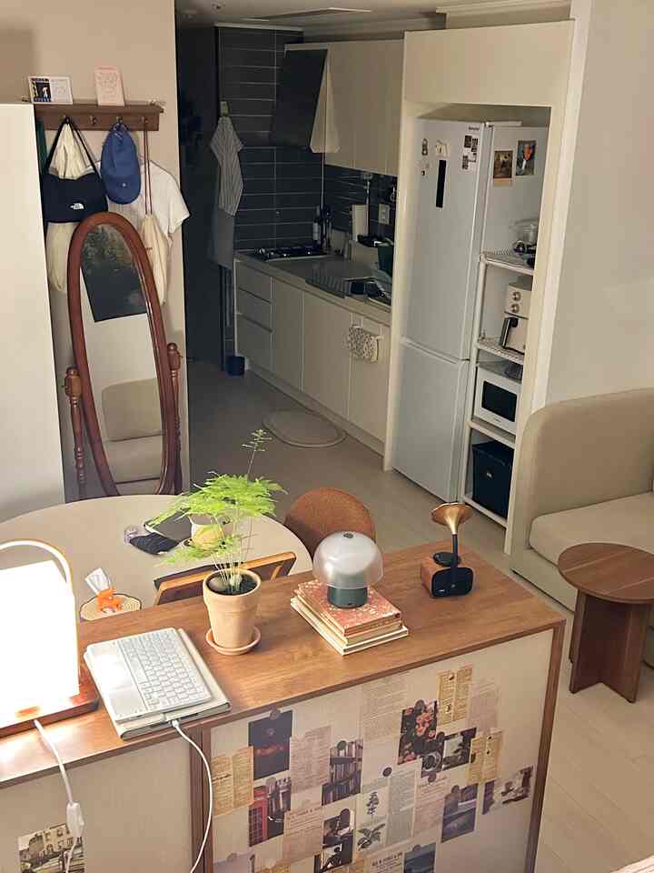 ホワイトと木目調が調和したワンルームのキッチンとリビング、ソファベッドと全身鏡が配置された印象的な空間
