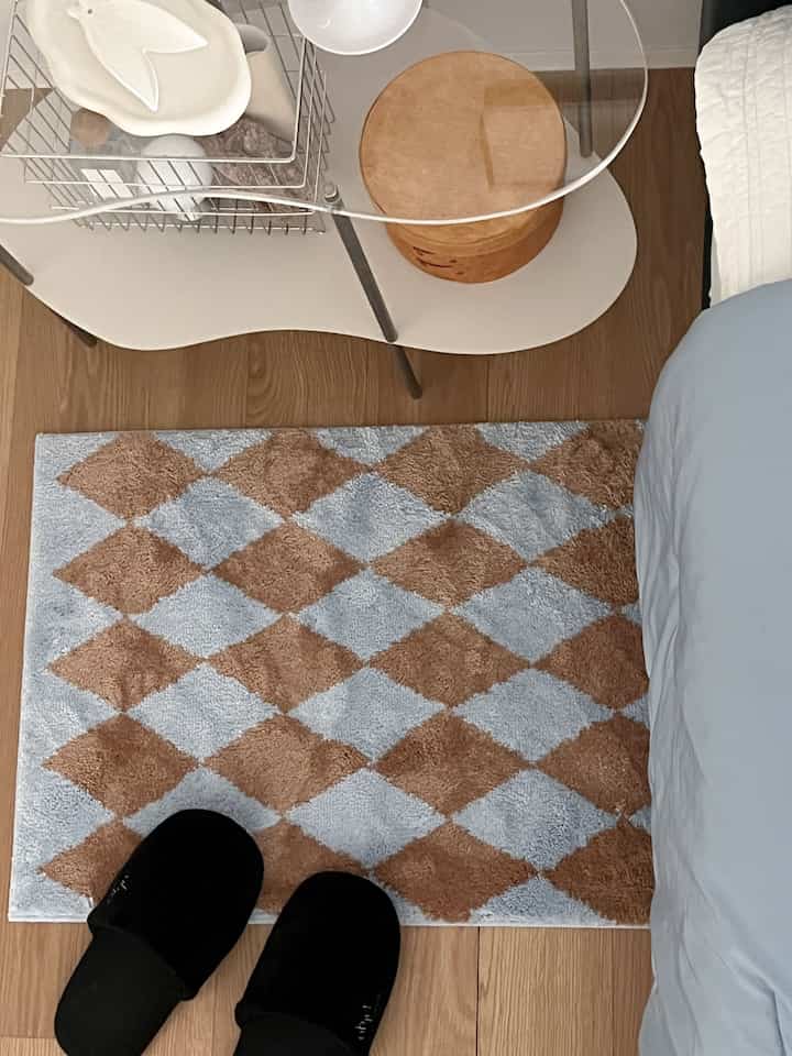 Cozy bedroom featuring a brown and blue checkered rug, wood flooring and a round wooden box adding warmth to the space