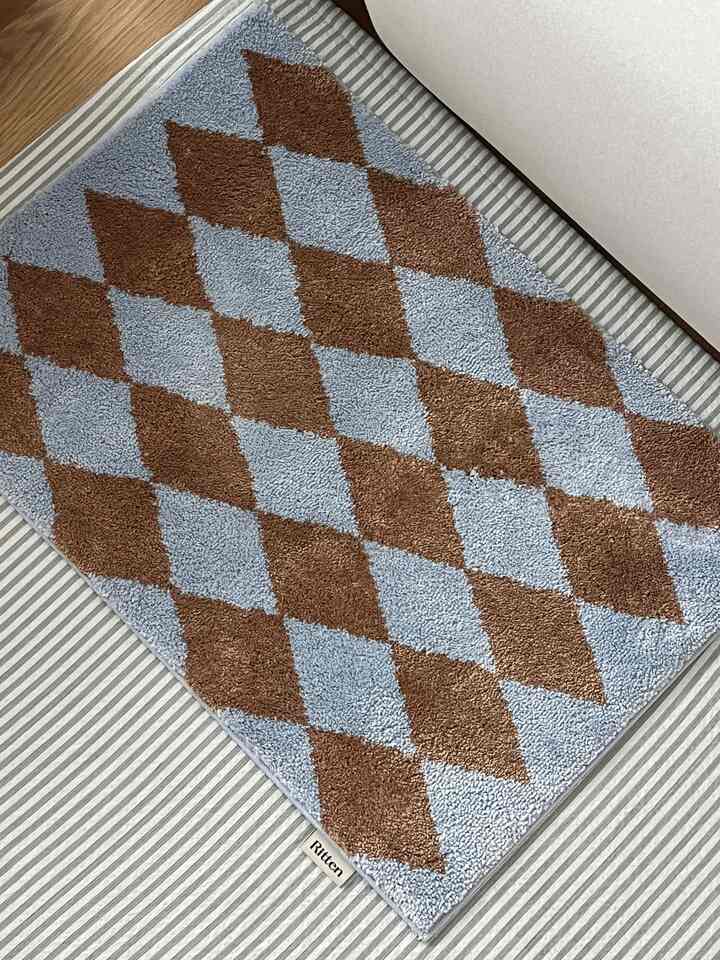 Blue and brown argyle pattern door mat placed on a striped floor, suggesting an entrance space