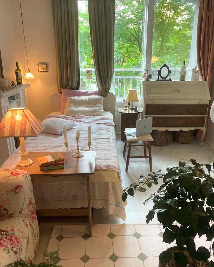 淡いピンクとオリーブグリーンの寝室、大きな窓とベッド、サイドテーブル、ヴィンテージ照明が配置された印象的な空間