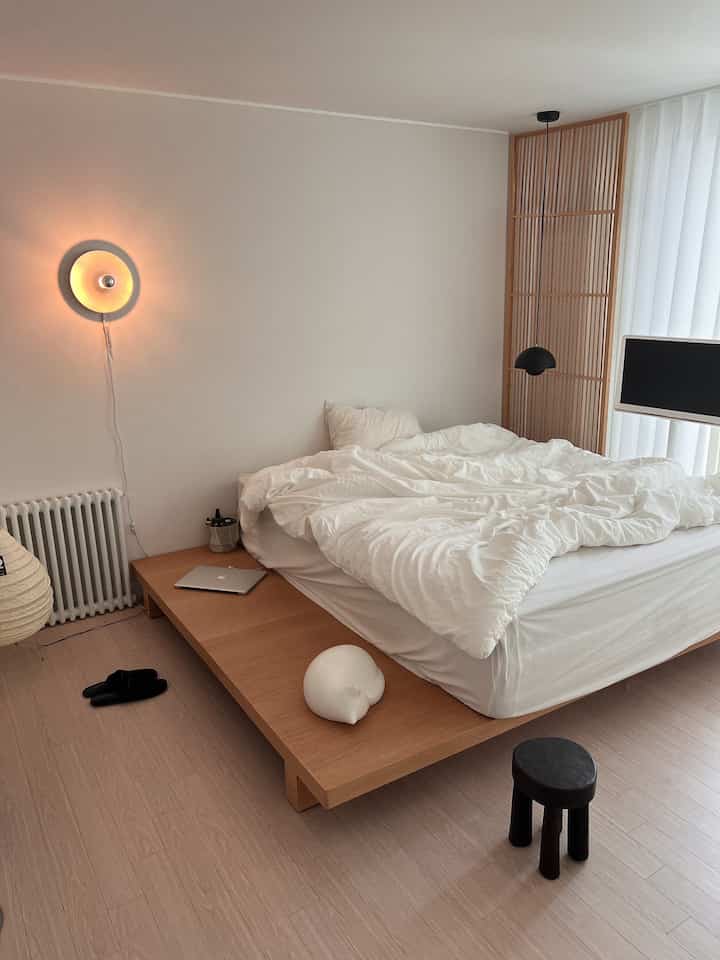 ナチュラルカラーと木目調の寝室、快適な木製ベッドと柔らかい白い寝具が配置されたモダンで雰囲気のあるインテリア