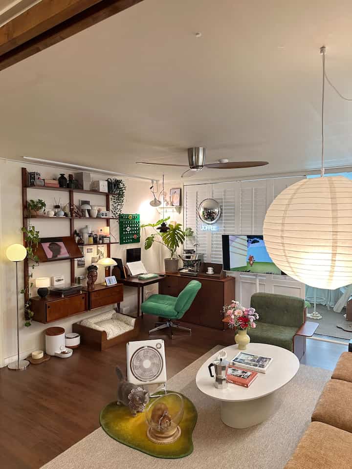 ブラウンの木目調とグリーンのアクセントソファが配されたヴィンテージスタイルのリビングルーム、シーリングファンや多様な照明がある雰囲気のあるインテリア