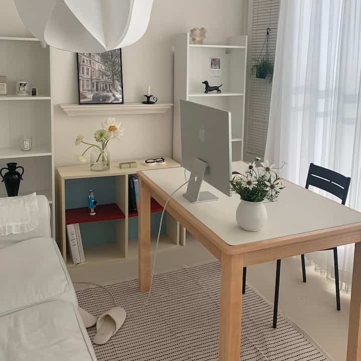 白と木目調を基調とした小さな書斎空間、机の上にAppleのiMacと花瓶があり、明るくミニマルな雰囲気