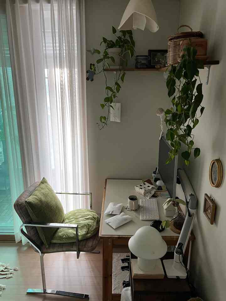 ナチュラルな色調のワンルーム書斎、木製の机と植物、窓際に置かれたアームチェアがある落ち着いた作業空間