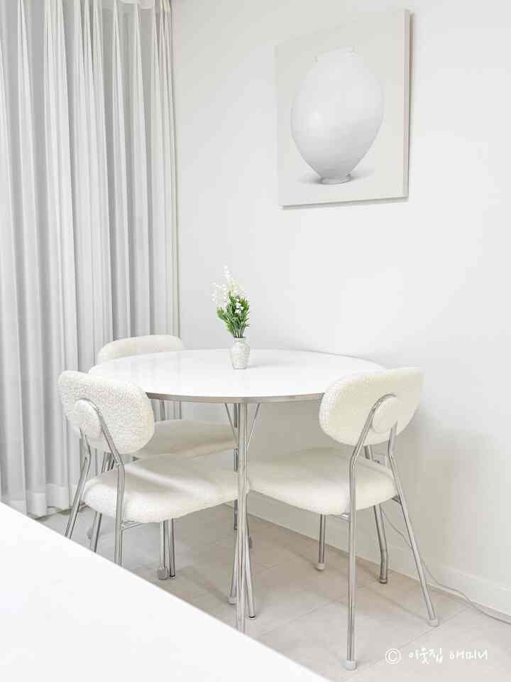 White-toned kitchen space featuring a round dining table and soft curved chairs in a clean, minimal interior