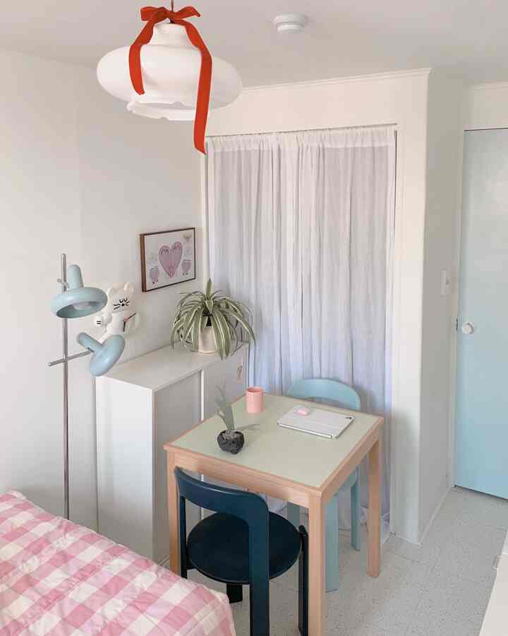 Small single-room in white and pastel tones, featuring simple furniture and pink bedding, creating a cozy atmosphere