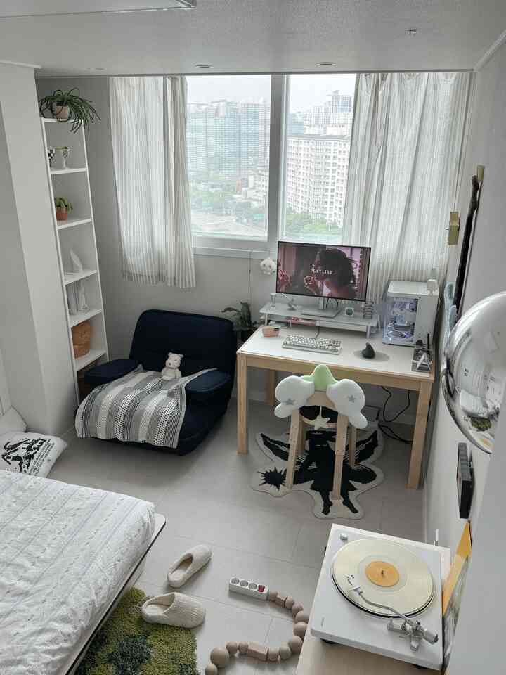 ホワイトとネイビーの色調が印象的な小さなワンルーム寝室、デスクと一人用ソファ、モニタースタンドが配置された雰囲気のあるインテリア