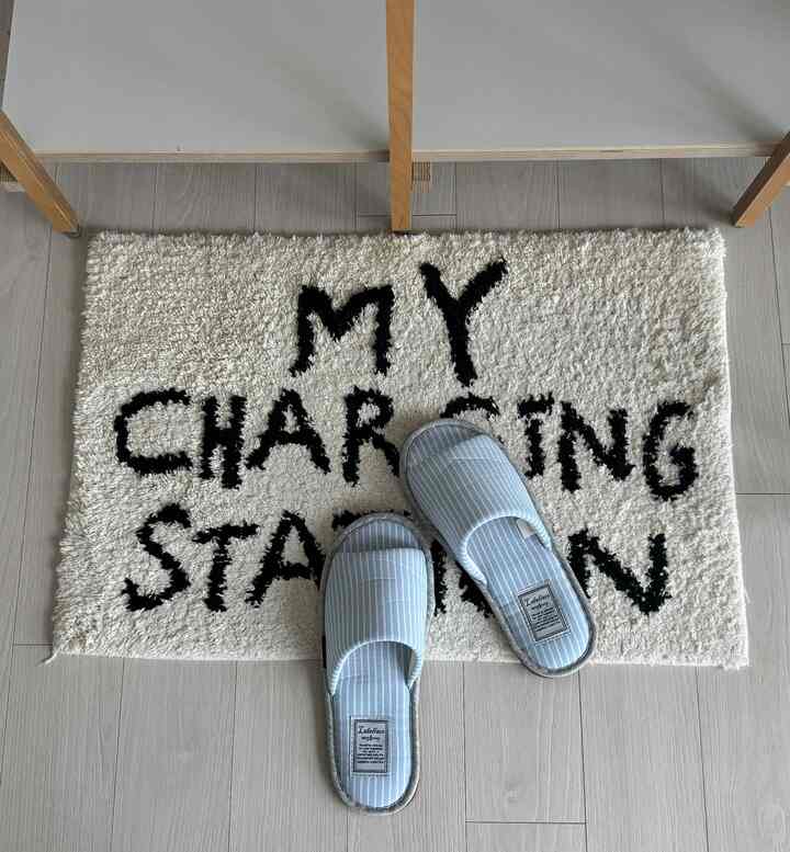 Entrance space with natural beige flooring, blue striped indoor slippers on a white bath mat featuring black lettering