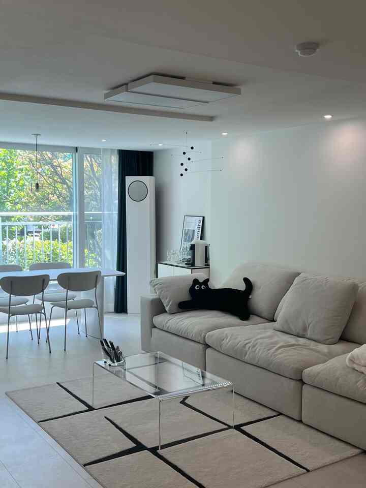 Bright white and beige living room featuring a transparent coffee table and a cat-shaped cushion in a natural modern style setting